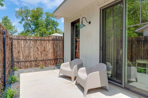 A patio with two white plastic chairs, a glass door, and a wooden fence.