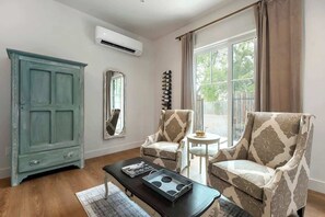 A living room with a teal cabinet, two patterned armchairs, a small round table, and a black coffee table with magazines.