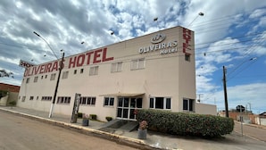 Exterior del Hotel Oliveira, con una fachada sencilla, un letrero llamativo, una pequeña entrada con escalones y un estacionamiento al frente.