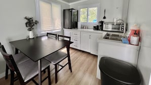 Una cocina moderna con armarios blancos, una mesa de comedor de madera y un bote de basura negro.