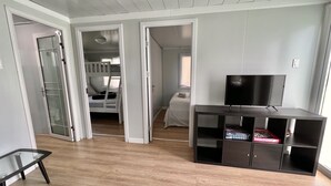 Una sala de estar moderna con un televisor sobre un mueble bajo, una mesa de vidrio y piso de madera.