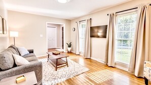A living room with a sofa, a coffee table, a TV, and a window with curtains. - Spacious Retreat Near Lake Hartwell, Clemson & Greenville! (Anderson)