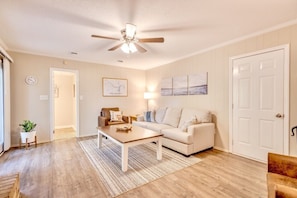 A living room with a ceiling fan, a sofa, a coffee table, and a door.