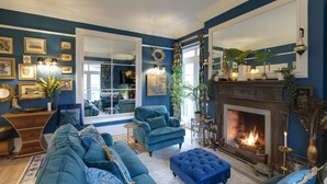 A living room with a fireplace, blue walls, and a large mirror. - Grand Historical Villa With Stunning Garden (Ross-on-Wye)