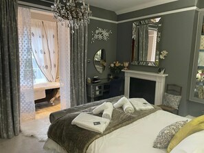 A bedroom with a bed, a mirror, a fireplace, and a chandelier. - Grand Historical Villa With Stunning Garden (Ross-on-Wye)