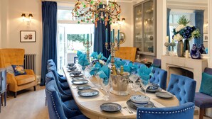 A formal dining room with a long table set for a meal, blue upholstered chairs, a chandelier, and a fireplace. - Grand Historical Villa With Stunning Garden (Ross-on-Wye)