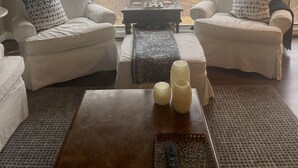 A living room with two white armchairs, a coffee table, and a view of a lake.