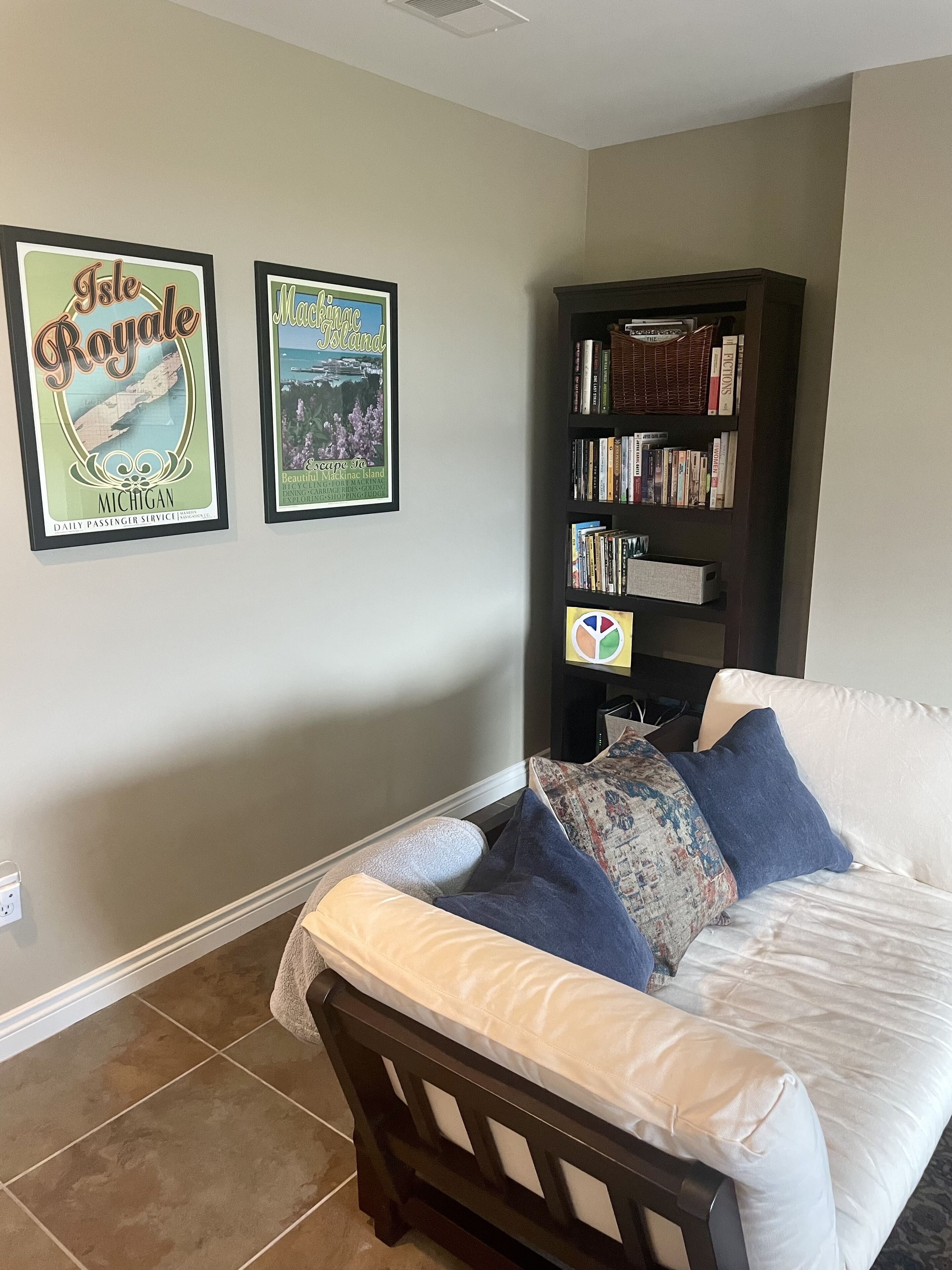 A bedroom with a bed, a bookshelf, and two framed posters on the wall.
