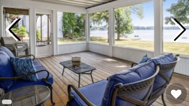 A covered outdoor seating area with blue cushioned chairs and a small table, overlooking a body of water.