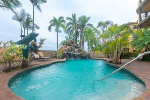 A swimming pool with a waterfall feature, surrounded by palm trees and lounge chairs. - Pineapple Villa 442 2 Bedroom Condo by RedAwning (Roatan)