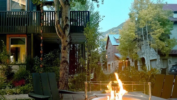 An outdoor fire feature surrounded by a metal railing, with a bench and a tree nearby.