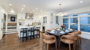 A modern kitchen with a central island, bar stools, and a dining table set for six.