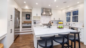 A modern kitchen with white cabinetry, a stainless steel range, and a marble island with bar stools.