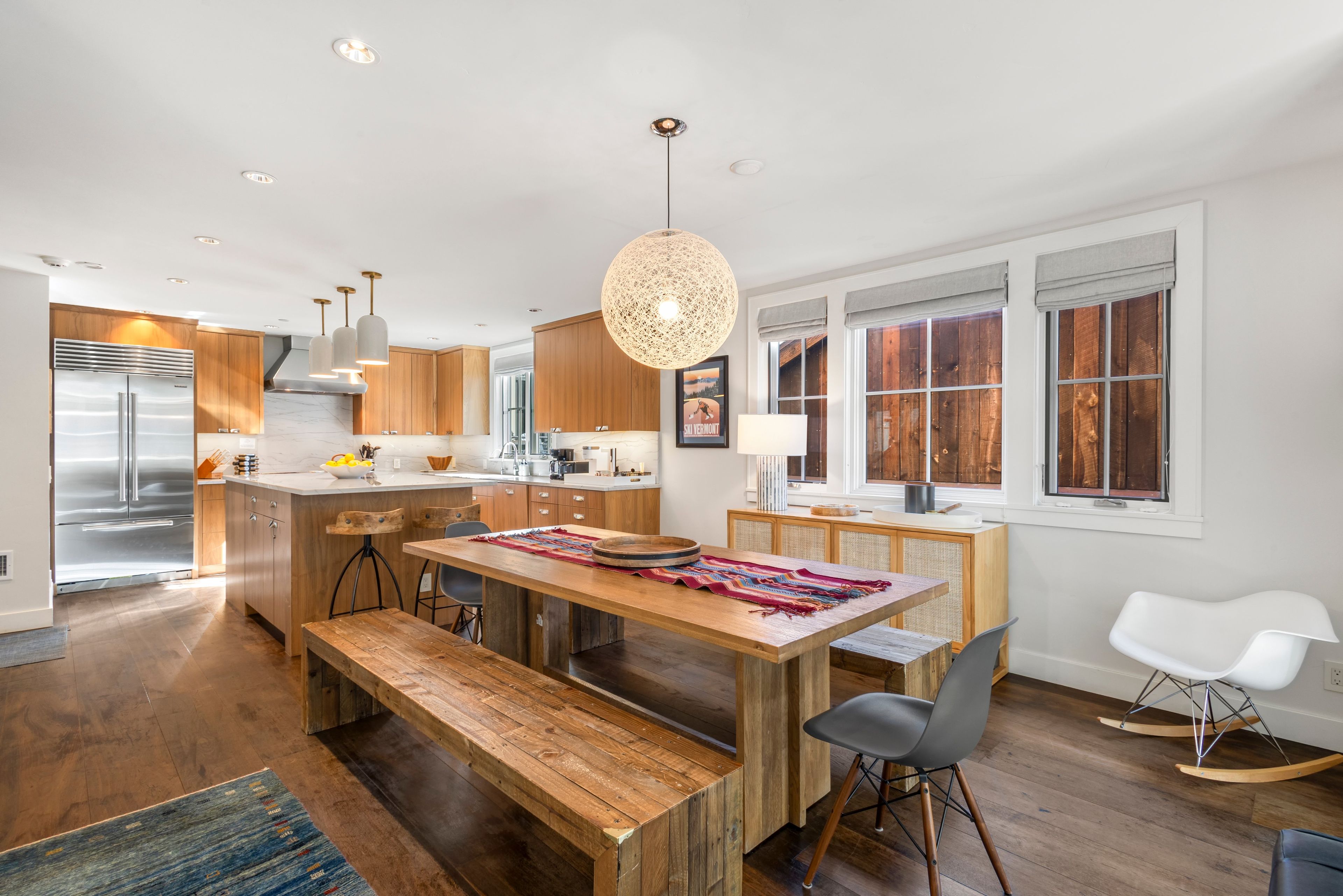 A modern kitchen with wooden cabinets, a stainless steel refrigerator, and a dining area with a wooden table and bench.