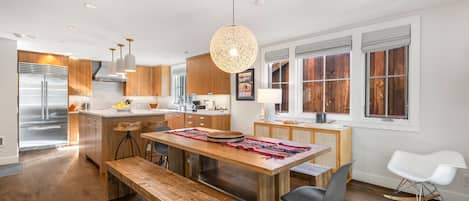 A modern kitchen with wooden cabinets, a stainless steel refrigerator, and a dining area with a wooden table and bench.