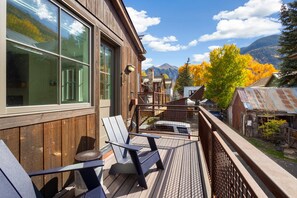 A wooden deck with outdoor seating, overlooking a mountainous landscape with autumn foliage.