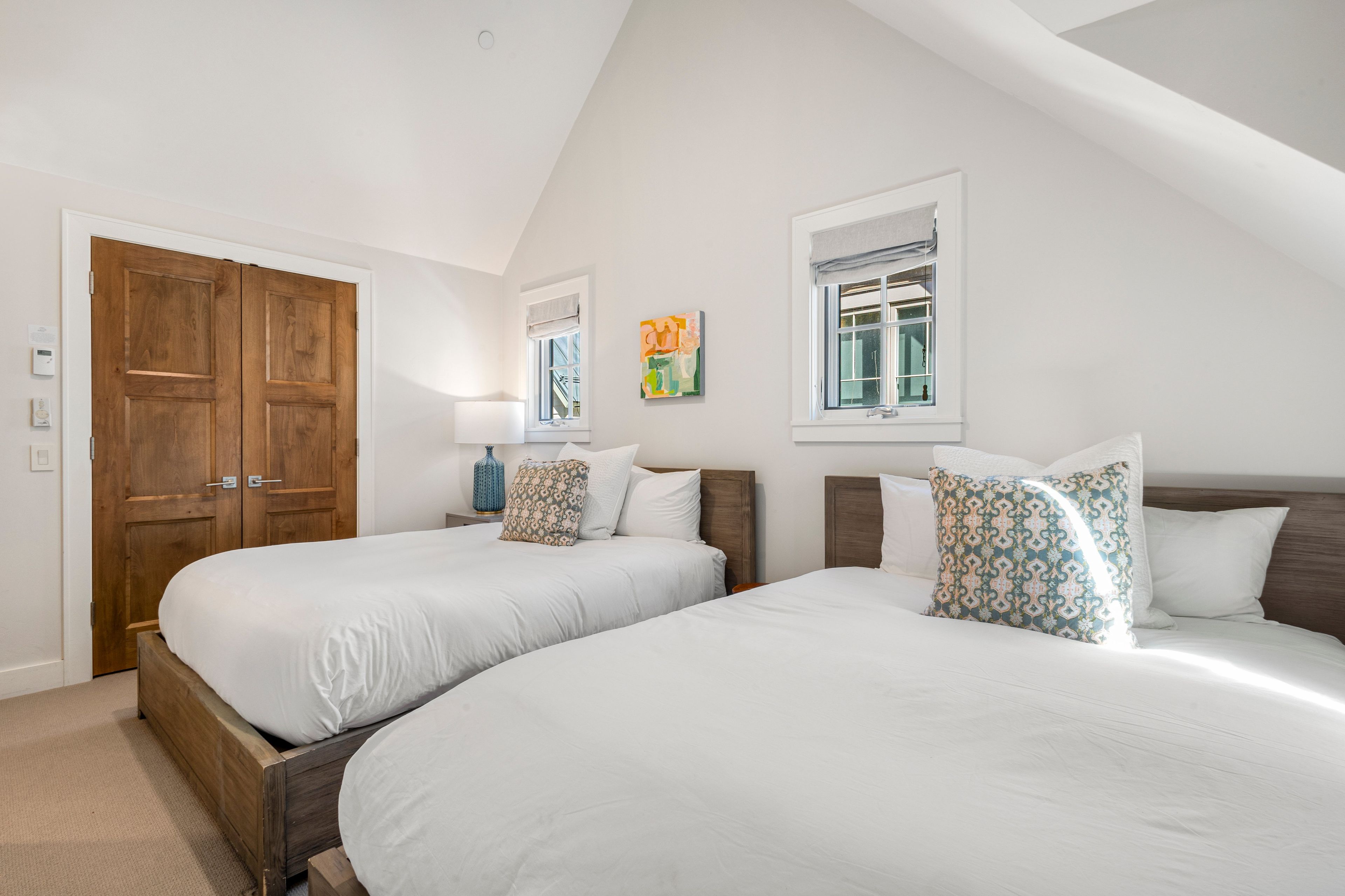 A bedroom with two beds, a wooden wardrobe, and a window with a view.