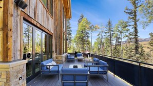 Eine Holzterrasse mit Sitzgelegenheiten im Freien und Blick auf Bäume und Berge.