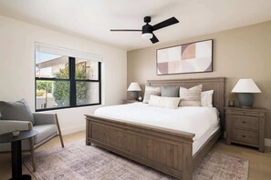 Une chambre à coucher avec un grand lit, un ventilateur de plafond, une fenêtre, un canapé et une table de chevet avec des lampes.