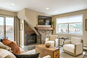 A living room with a fireplace, a television, and a view of the outside.