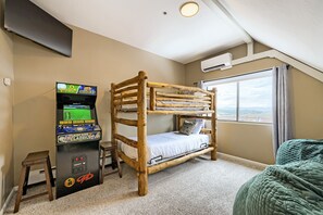 Ein Etagenbett mit Holzrahmen, eine Spielkonsole, ein kleiner Hocker und ein Fenster mit Blick.