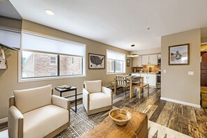 A modern living room with two white armchairs, a wooden coffee table, and a dining area with a wooden table and chairs. - Village Loft 31 At Park City Mountain 2 Bedroom Condo by RedAwning (Park City)