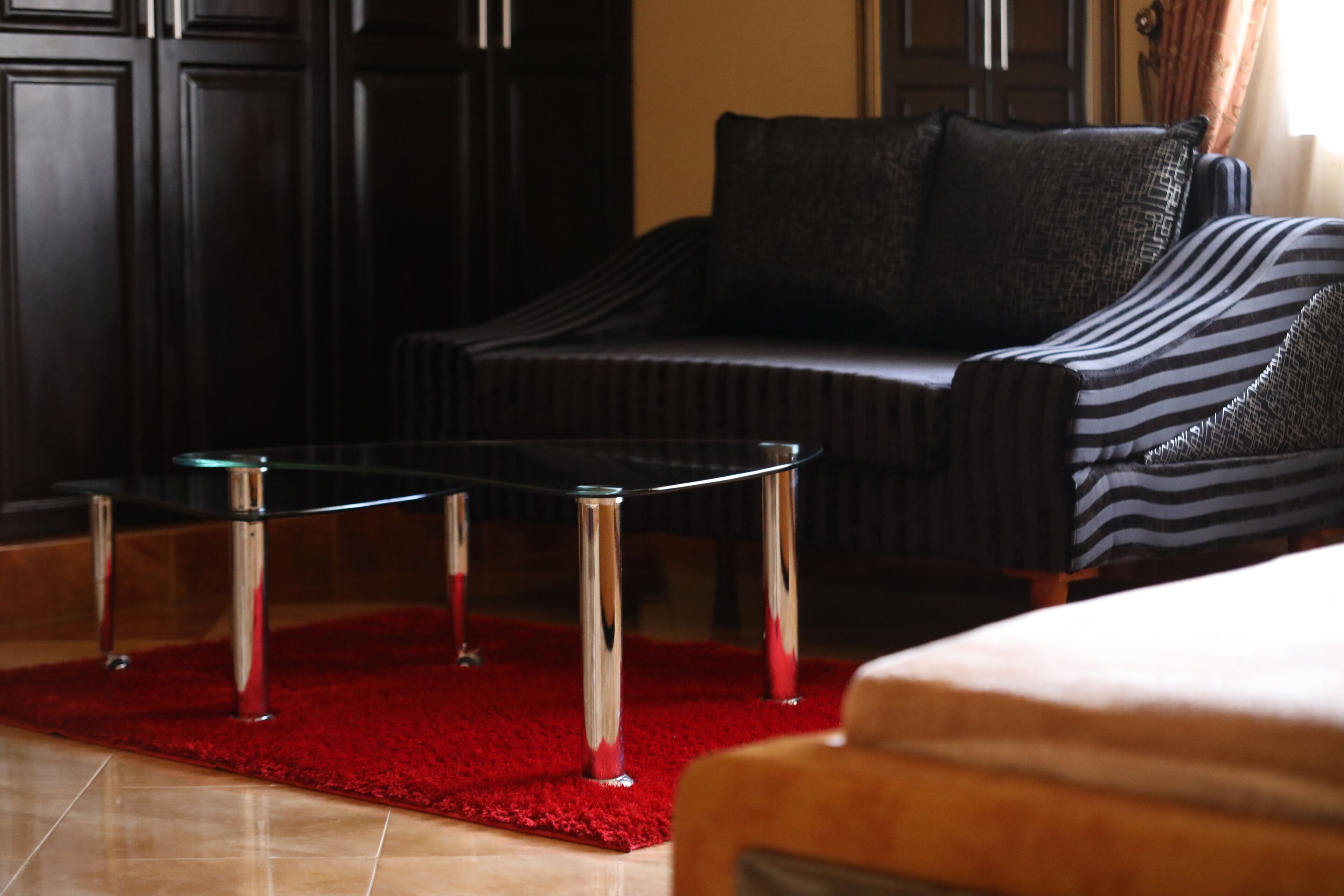 A modern living room with a dark-colored sofa, a red rug, and a glass coffee table.