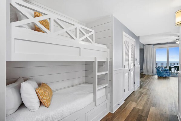 A modern hotel room with a bunk bed, a balcony with a view, and a blue chair.