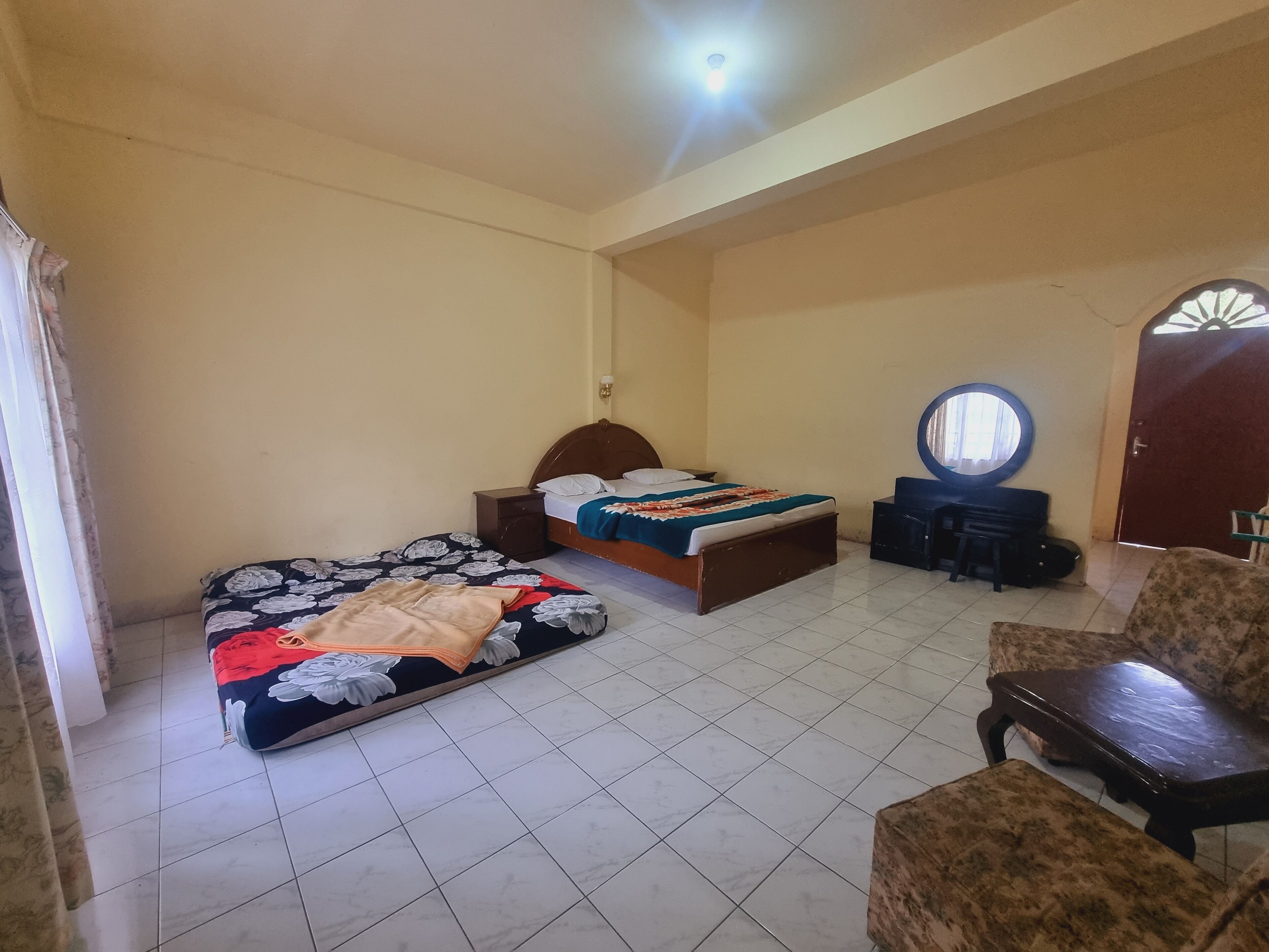 Ein Schlafzimmer mit zwei Betten, einem Sessel, einem kleinen Tisch und einem Spiegel.