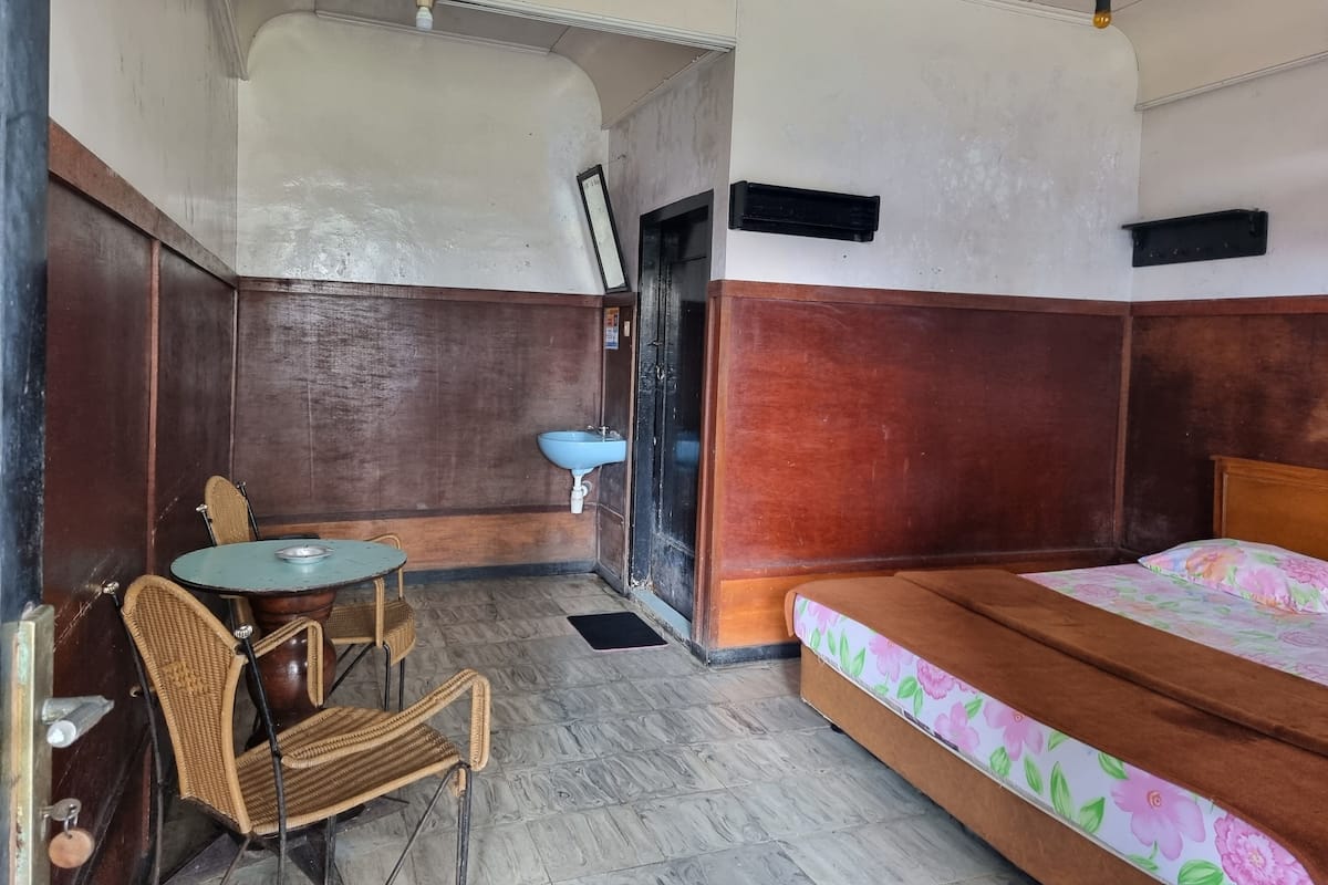 Um quarto com uma cama, uma mesinha com cadeiras, uma pia e uma porta.