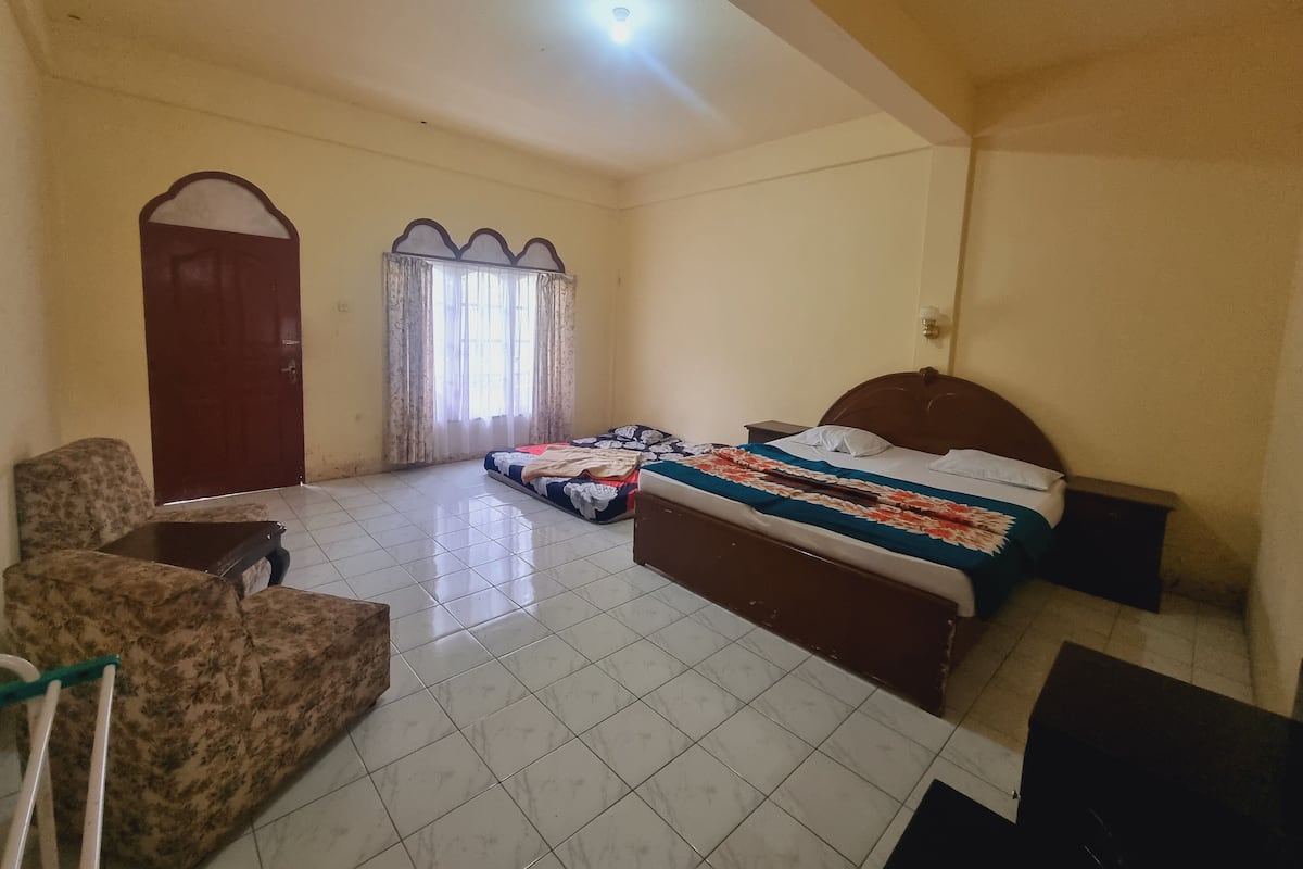 Quarto com cama, cadeira, escrivaninha e janela com cortinas.
