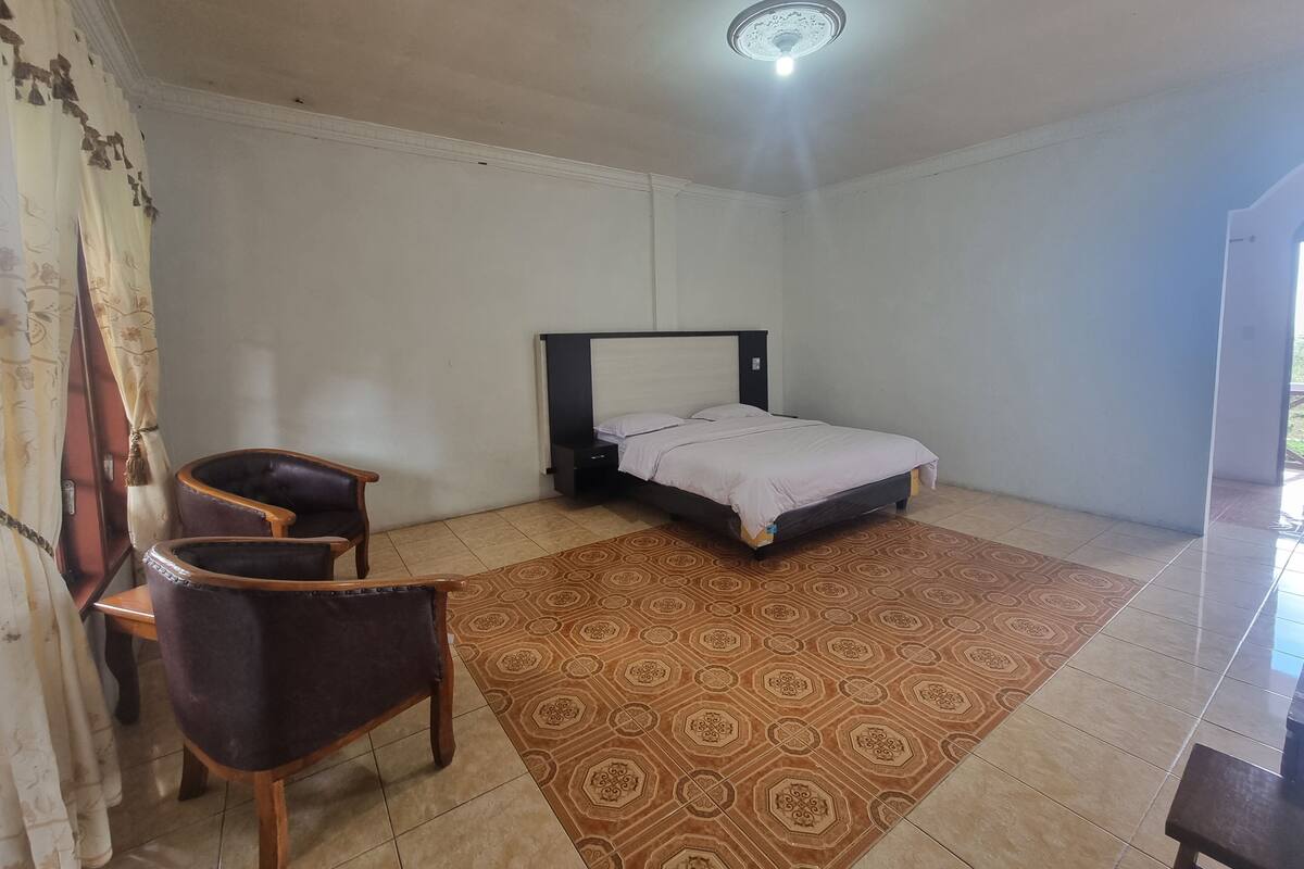 Quarto com cama, uma cadeira e tapete estampado.
