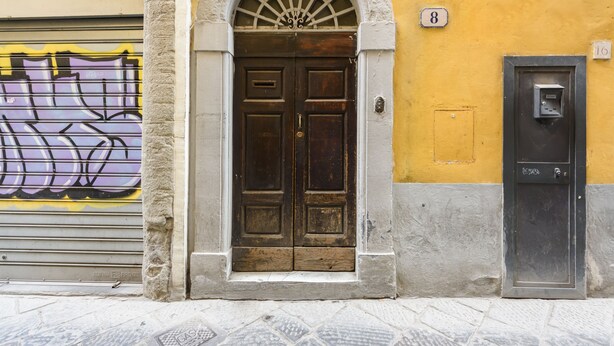 A building facade with a double wooden door, a number 8 sign above it, and a utility box with a number 16 sign. - Madame Betta by Mmega (Florence)