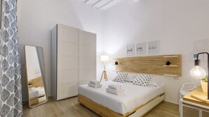 A modern bedroom with a wooden bed, a large mirror, a wardrobe, a bedside table with a lamp, and motivational wall art. - Madame Betta by Mmega (Florence)