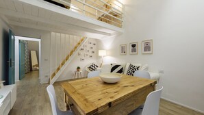 A dining area with a wooden table, white chairs, a staircase, and a wall with framed pictures. - Madame Betta by Mmega (Florence)