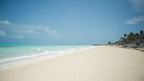 Une plage à l’eau turquoise et limpide, un rivage sablonneux et un promontoire rocheux parsemé de palmiers.