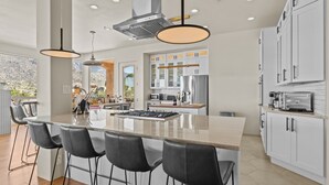 Cocina moderna con una isla grande, taburetes de bar, armarios blancos y vistas a un paisaje montañoso.