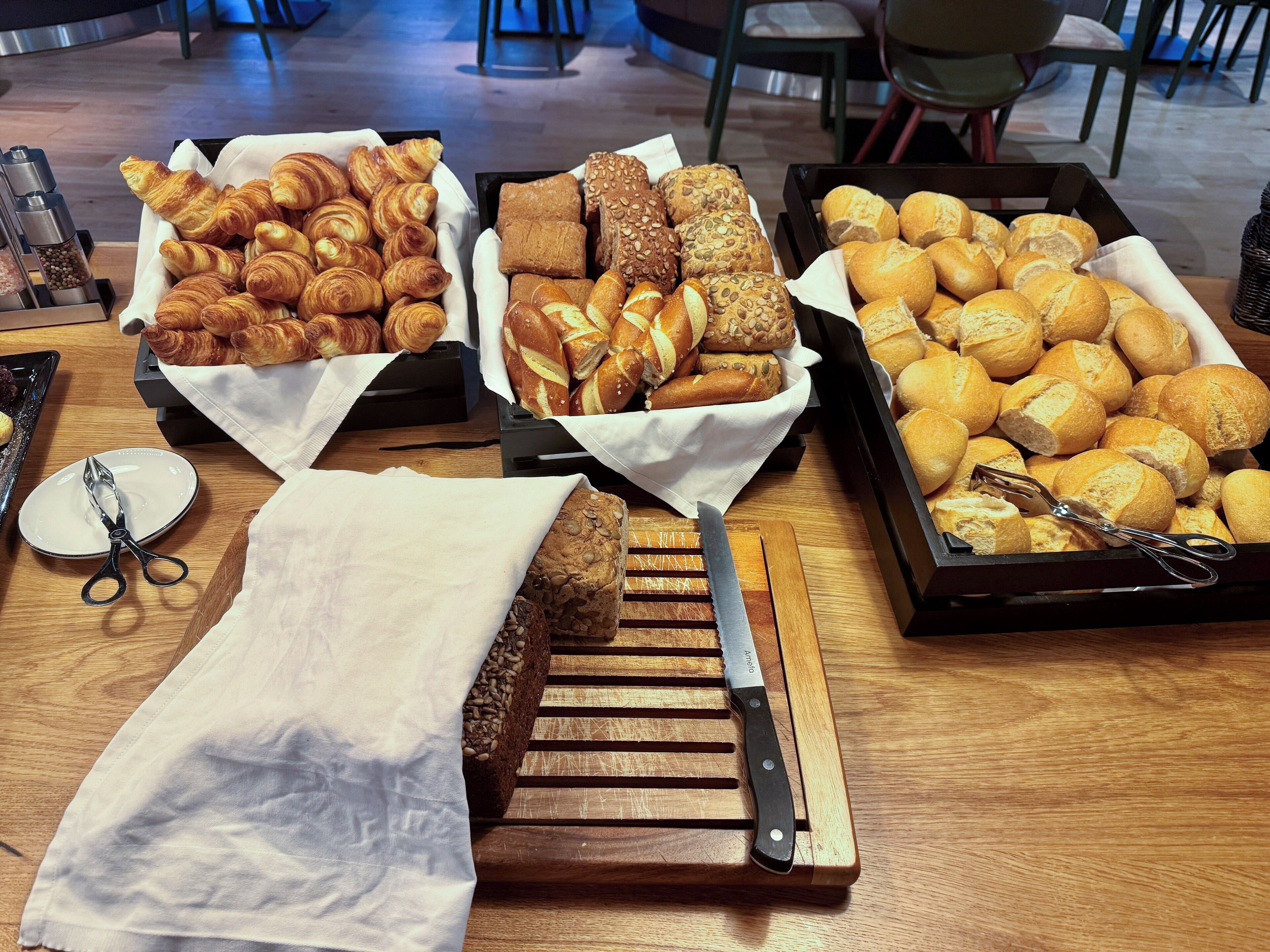 A variety of baked goods displayed on a wooden table, including croissants, bread rolls, and baguettes.