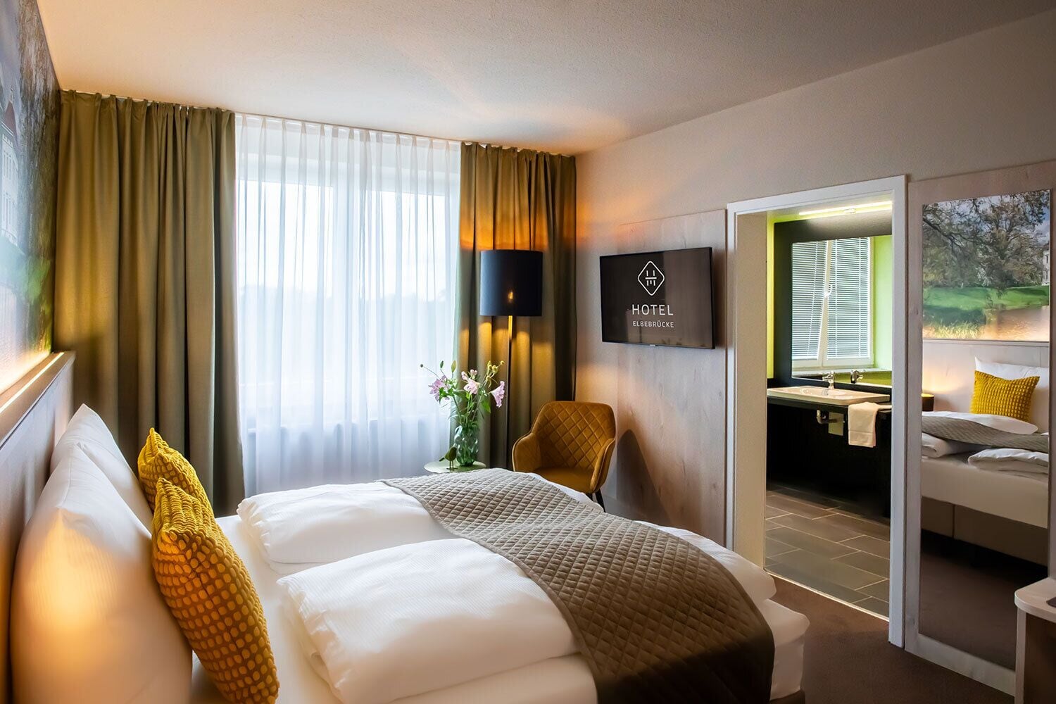 A hotel room with a bed, a TV, a chair, and a view of the outside.