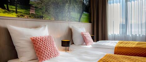 A hotel room with two beds, a large window with curtains, a wall mural, and a bedside table with a lamp.