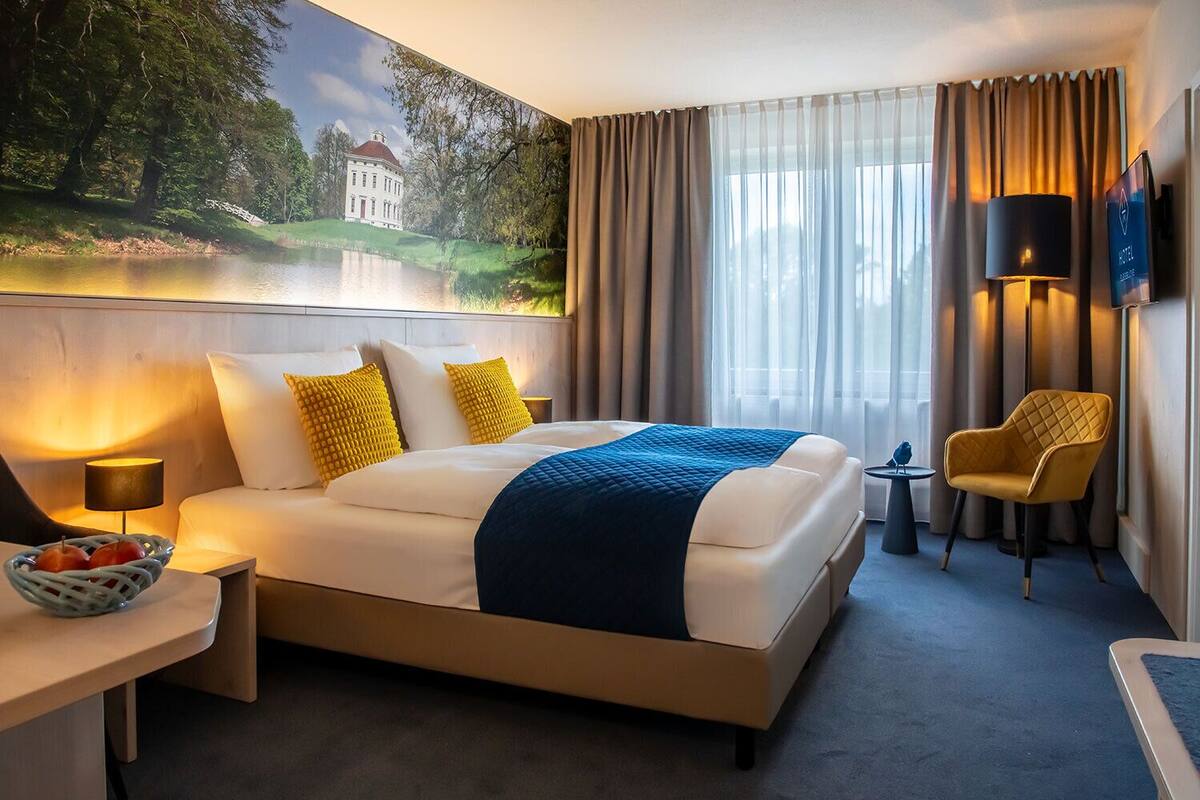 Ein Hotelzimmer mit einem großen Bett, einem Schreibtisch mit Lampe, einem Sessel und einem Fernseher.