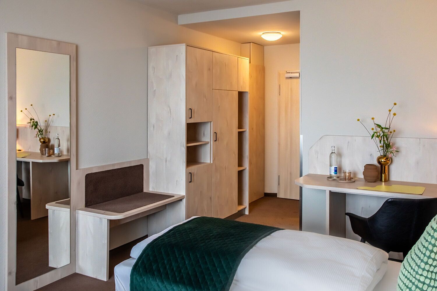 A hotel room with a bed, a desk, a chair, a wardrobe, and a mirror.