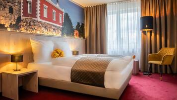 A hotel room with a large bed, a nightstand with a lamp, a chair, and a mural on the wall.