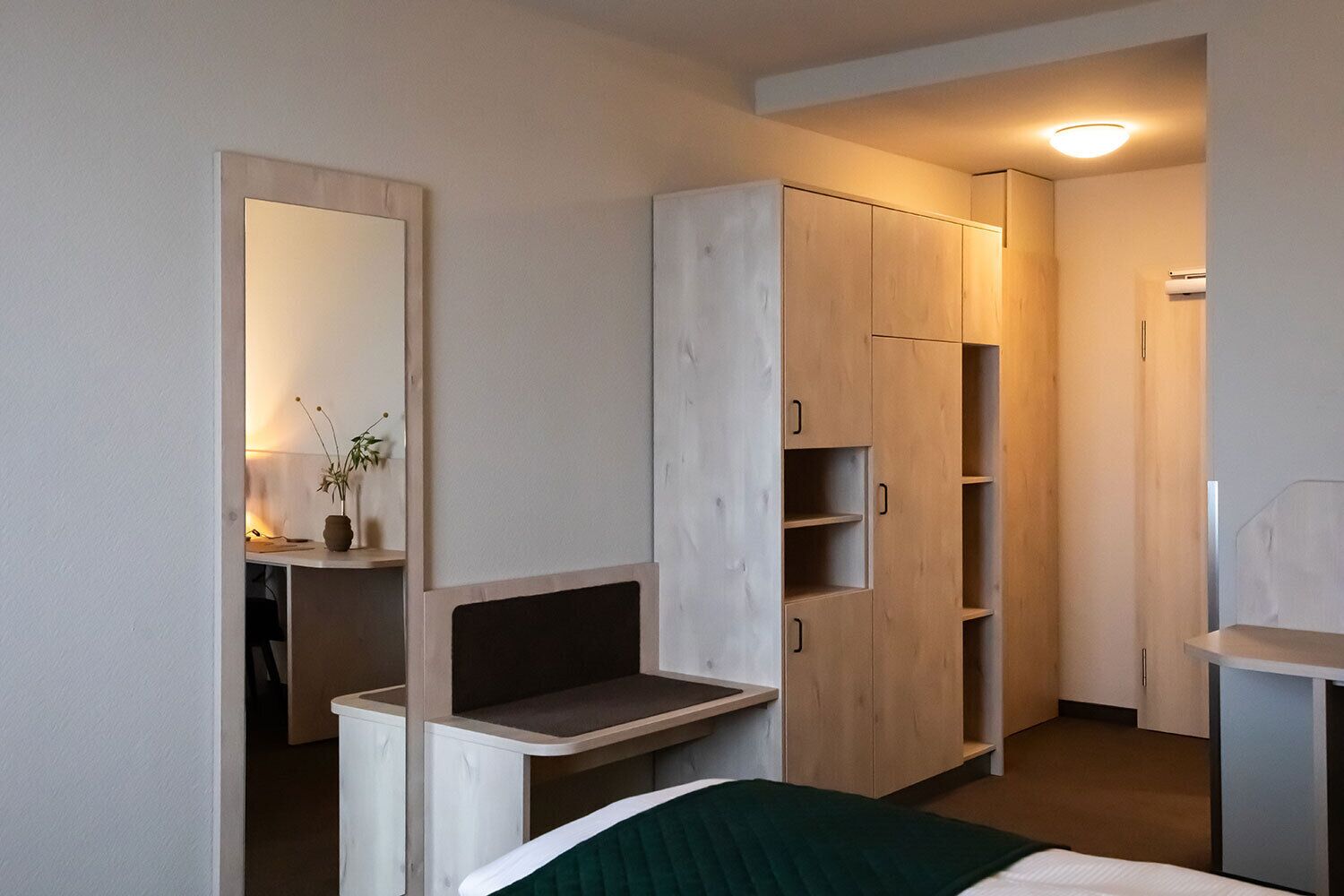 Une chambre à coucher comprenant un lit, une table de chevet, un miroir, une armoire et un petit bureau avec une chaise.
