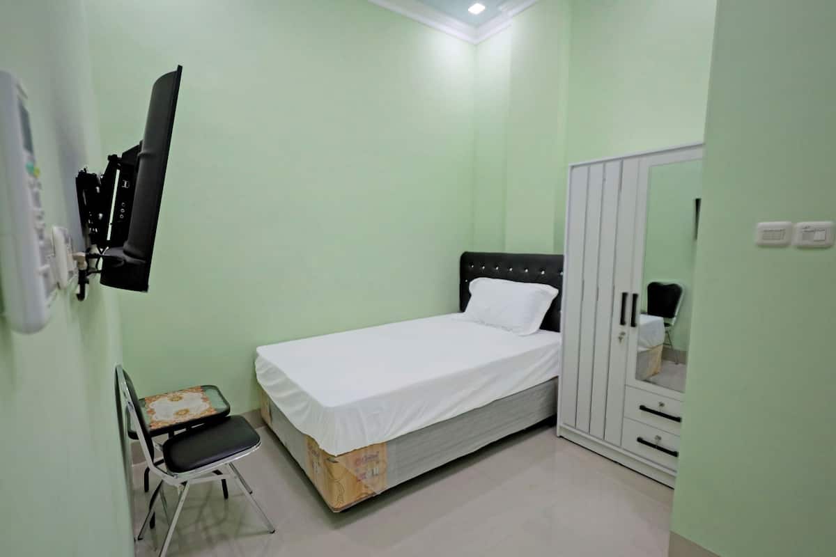 A small, clean room with a single bed, a chair, a wardrobe, and a mirror.