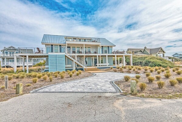 A modern coastal house with a spacious deck, a covered outdoor area, and a landscaped driveway.