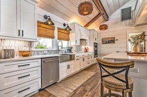A modern kitchen with white cabinetry, a wooden floor, and a dining area with a wooden chair.