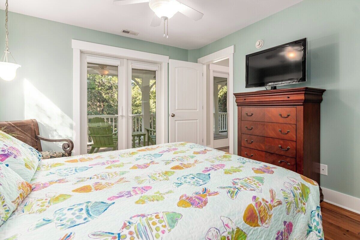 Une chambre à coucher comprenant un lit, une commode, un téléviseur et une porte-fenêtre coulissante donnant sur un espace extérieur.