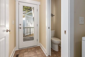 Enter a serene space with a bathroom featuring a toilet and sink, flanked by a window offering a view of a deck and tree.