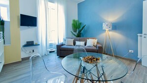 A modern living room with a glass dining table, a brown sofa, and a blue accent wall.